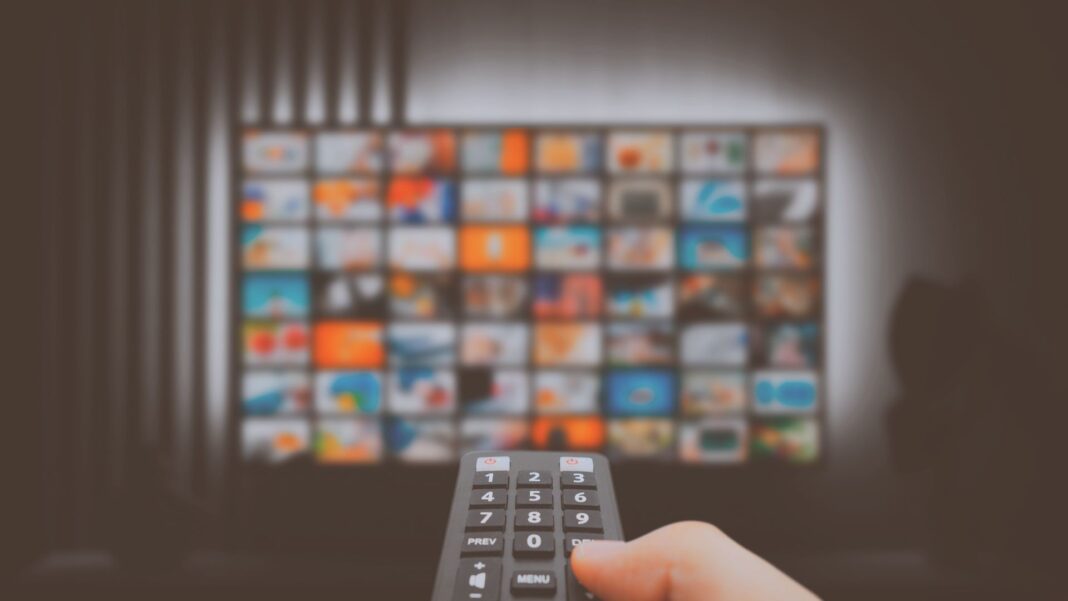 Familia hispana viendo televisión y streaming, combinando pantallas grandes, laptops y dispositivos móviles, reflejando su conexión con medios digitales y tradicionales.