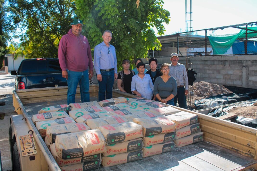 Ismael Pérez Pavía y Héctor Gallardo Carrera entregan sacos de cemento para la construcción de salones comunitarios en la capilla de Nuestra Señora de Guadalupe, en Los García, Meoqui.